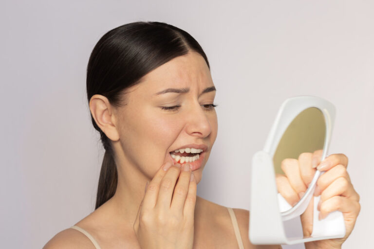 Young pretty caucasian woman looking at her red gums on her lower jaw in the mirror. She suffering from gingivitis, gum inflammation. Dental care. Dentistry. Oral care